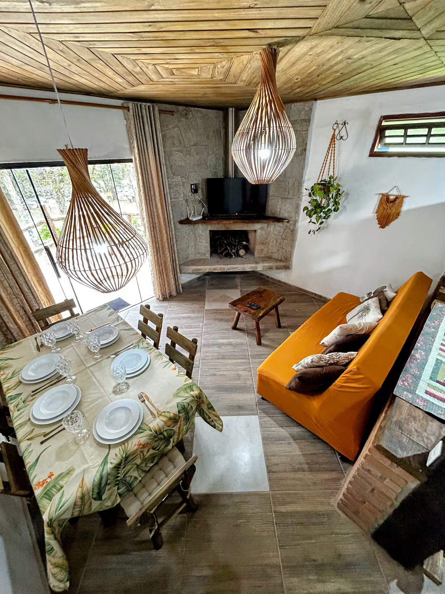 Sala com lareira de pedra, sofá laranja e mesa de jantar com vista para a varanda